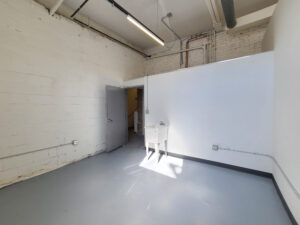 A bright studio space with bright sunlight against white drywall and white-painted brick, with a sink in one corner