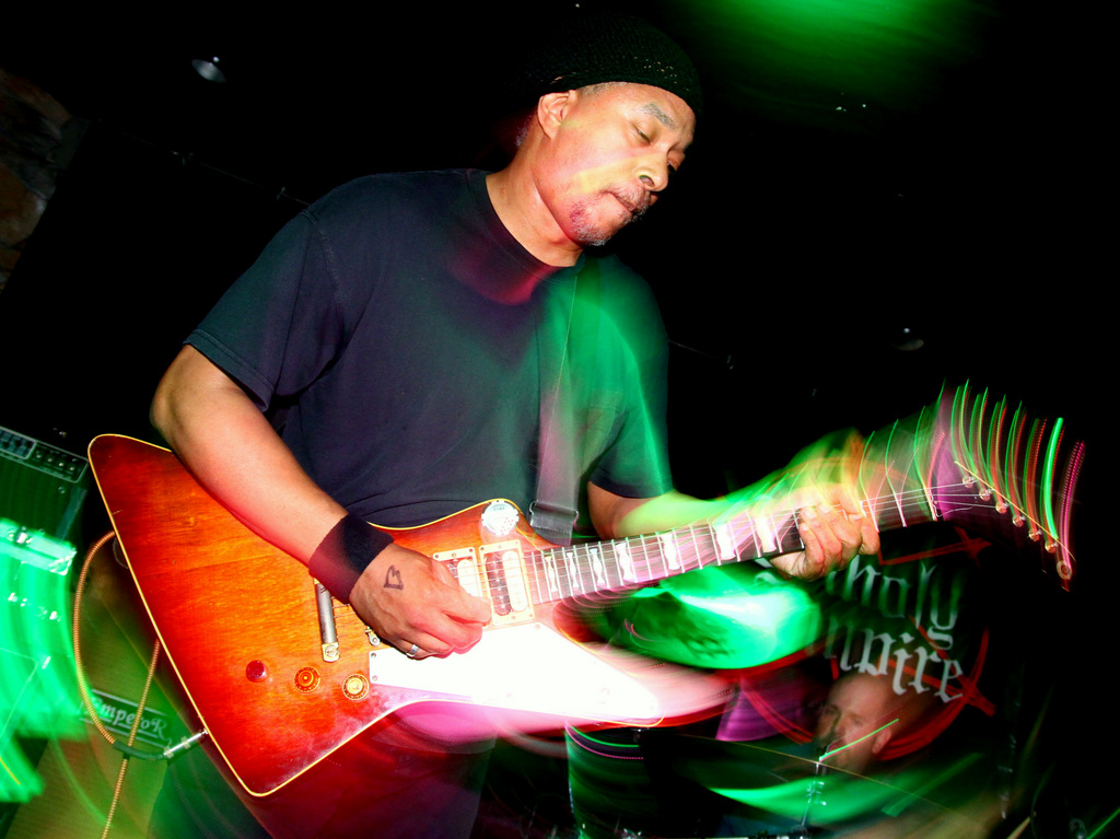 A rock musician playing a Gibson Explorer (or asymmetrical star-shaped) electrical guitar on a stage under green lighting
