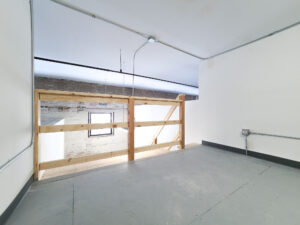 A studio loft view looking down a studio space with dry whitewall abutting a brick exterior wall with a window set inside